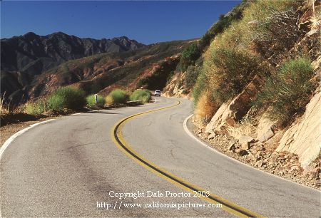 Scenic photos of highways national forest mountain road curves outdoors to Santa Barbara yellow lines winding down long grade in canyon, blue sky, picture of Southern California coastal region